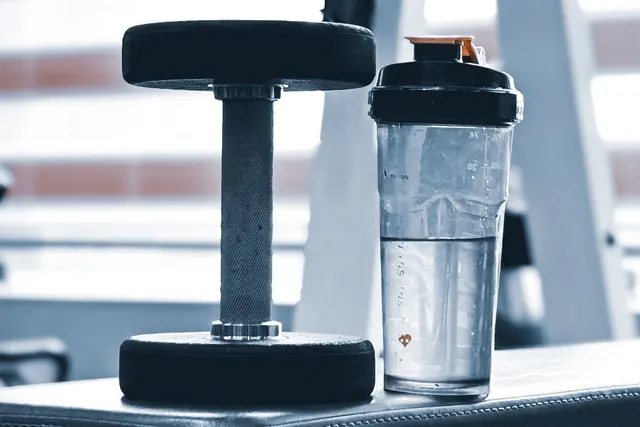 Uno shaker trasparente accanto a un manubrio su una panca in palestra
